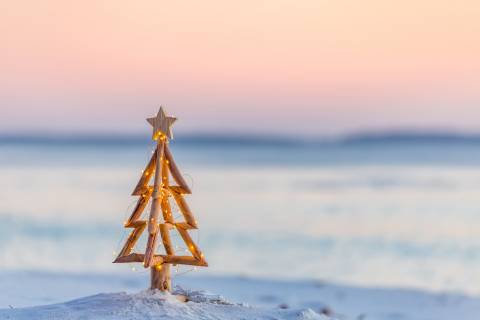 small, decorative wooden Christmas tree in the sand on the beach